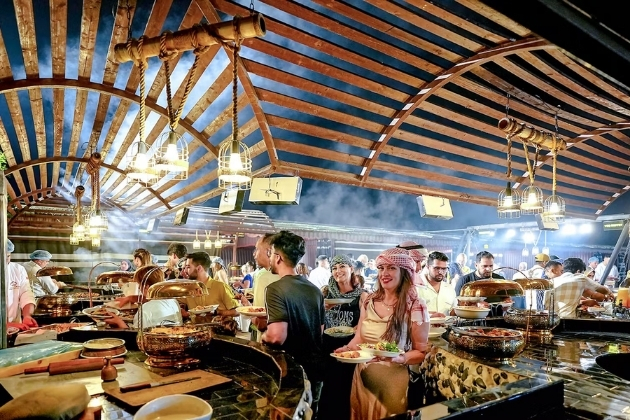 Guests enjoying a traditional Arabian BBQ buffet dinner under a wooden canopy during a Dubai desert safari