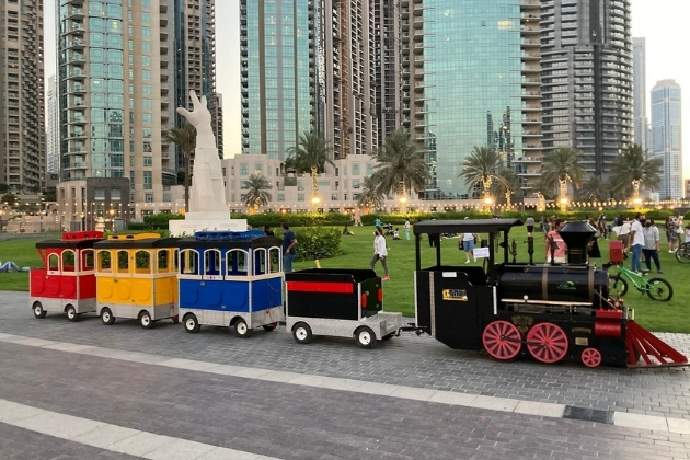 Colorful mini train parked in Burj Park, with families enjoying the green space surrounded by modern skyscrapers in downtown Dubai.