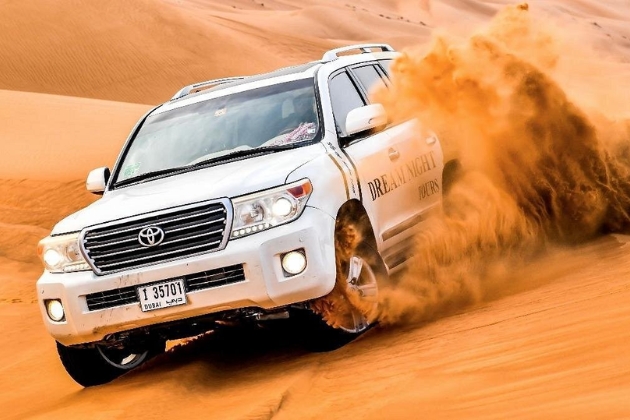 4x4 SUV kicking up sand while dune bashing across the Dubai desert's golden dunes