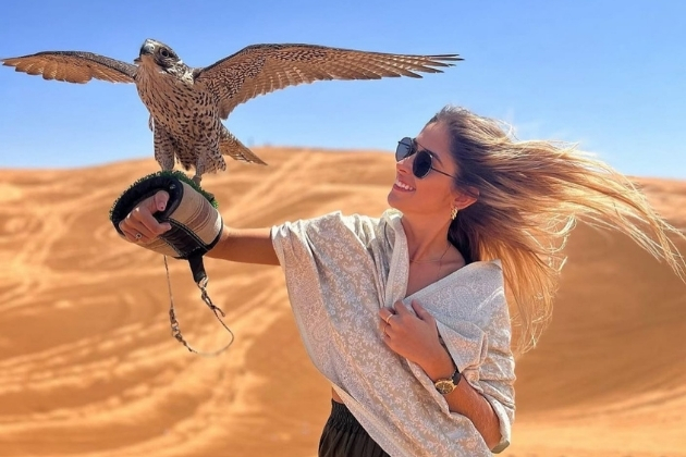 Tourist holding a falcon on her gloved hand during a falconry experience in the Dubai desert