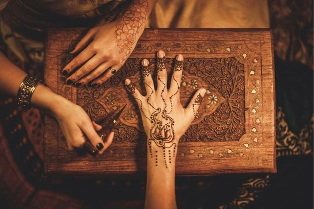 Artist applying intricate traditional henna design on a woman’s hand at a desert safari camp in Dubai