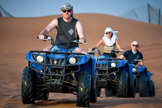 Adventurous tourists riding quad bikes across the Dubai desert during an off-road safari adventure