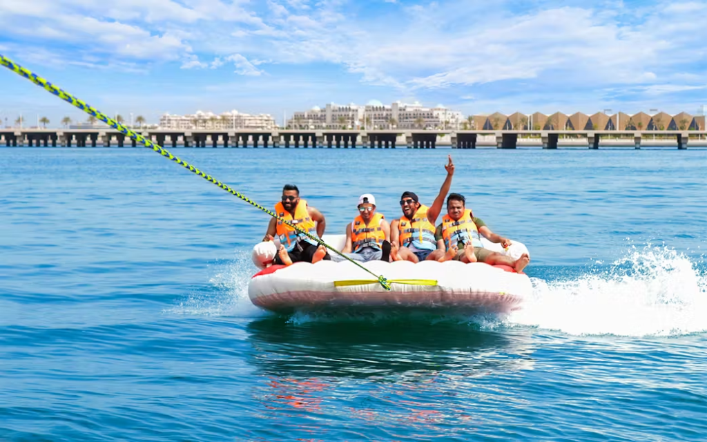 Four friends having fun on a water tube ride being pulled across the blue waters in Dubai.