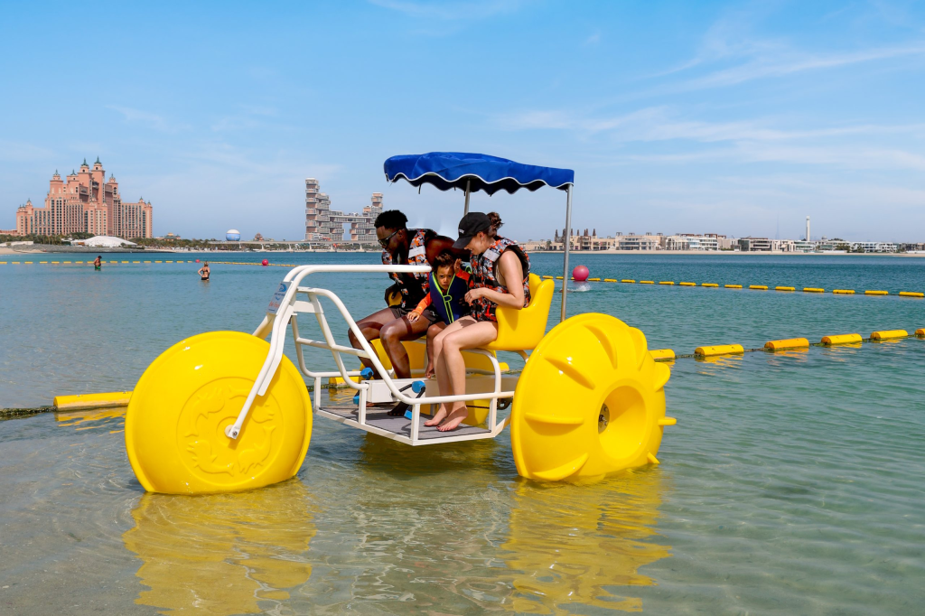 Group enjoying a fun water trike ride with bright yellow wheels in the shallow waters near Atlantis The Palm, Dubai.